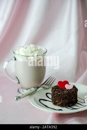 un gâteau avec de minuscules copeaux de chocolat et un coeur rouge et rose chocolat. et une tasse de chocolat chaud avec crème fouettée. friandises sucrées! Banque D'Images