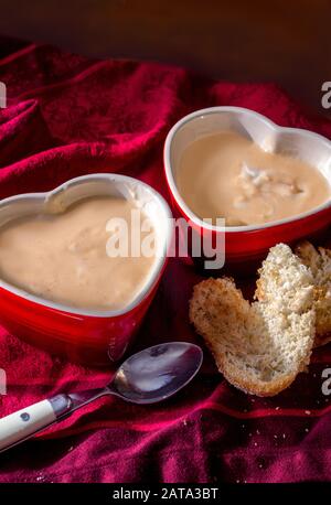 Soupe crémeuse aux poireaux de pommes de terre chaudes, servie dans des bols rouges en forme de coeur avec des tranches de pain grillées en forme de coeurs Banque D'Images