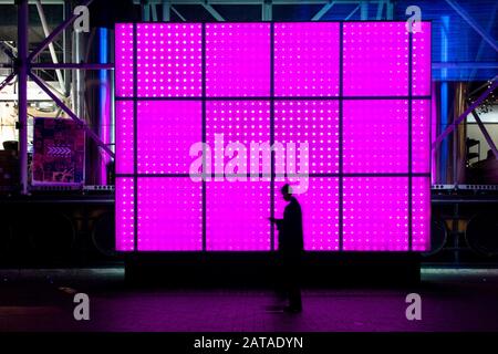 Un marcheur est silhouetté contre un mur rose de lumières sur la South Bank à Londres Banque D'Images