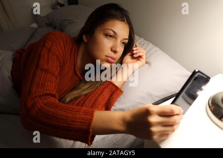 Une fille souffrant d'insomnie vérifie le temps au téléphone. Jeune femme éveillée tard dans la nuit à l'aide d'un smartphone allongé dans le lit. Dépendance à l'Internet, abus mobile Banque D'Images