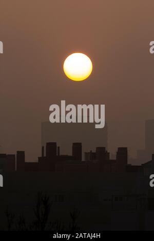 Coucher de soleil avec un grand soleil rond sur une ville avec brouillard Banque D'Images