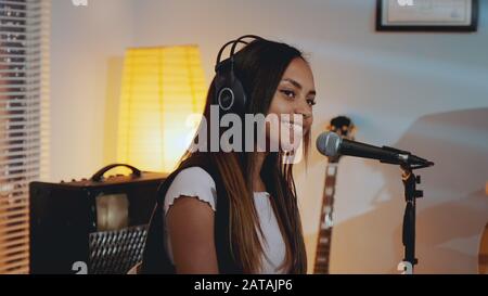 Gros plan sur une belle fille souriante dans un casque chantant sa chanson préférée sur la répétition en studio à la maison le soir. Banque D'Images