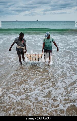 Deux hommes Sri-lankais transportant du poisson dans un panier bambo sur la plage de Trincomalee et le lavant dans l'océan. Banque D'Images