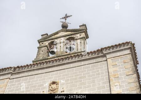Clocher d'une église avec une croix métallique sur le dessus et détails sculptés en pierre sur la façade, à l'ouest de l'Espagne, à Serradilla (Caceres) Banque D'Images