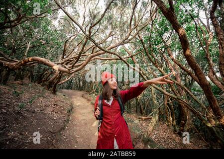 Portrait d'une heureuse femme vêtue de façon décontractée en chemise rouge et chapeau randonnée dans la belle forêt tropicale, montrant vers l'avant en voyageant sur l'île de Tenerife, Espagne Banque D'Images