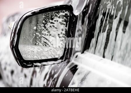 Gros miroir de voiture noire dans le savon. Concept de voiture de lavage Banque D'Images