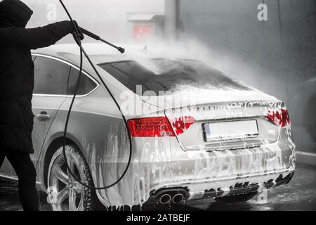 Homme laver sa voiture grise sous l'eau haute pression à l'extérieur. - vue arrière Banque D'Images