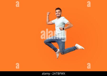 Portrait complet d'un homme brunette d'inspiration positive avec barbe en sneakers, tenue denim sautant dans l'air ou courir rapidement. Prise de vue en studio intérieure Banque D'Images