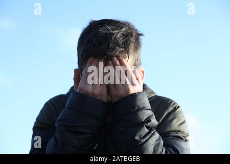 Un jeune garçon de 12 couvre son visage boueux avec ses mains, face à la caméra Banque D'Images