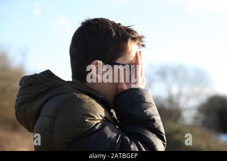 Un jeune garçon de 12 couvre son visage boueux avec ses mains, profil latéral Banque D'Images