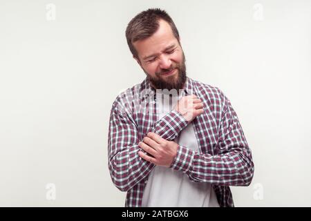 Dommages aux mains, blessures. Portrait d'un homme malsain barbu dans un bras de frottement décontracté de chemise de plaid, souffrant d'un poignet douloureux et de polyarthrite rhumatoïde. Banque D'Images