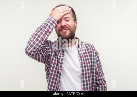 Mémoire incorrecte. Portrait d'un homme barbu embarrassé et obsé dans un maillot de plaid décontracté faisant un geste facepalm, se sentant triste et regrettable, se blâmant lui-même. Banque D'Images