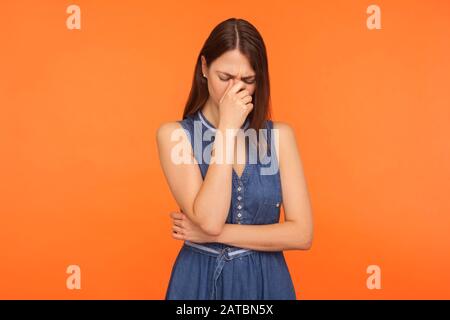 Frustrée, triste femme brunette dans la robe denim pleurant, essuyant les larmes, se sentant déprimée, bouleversée par la perte, le deuil, les émotions désespérées. Banque D'Images