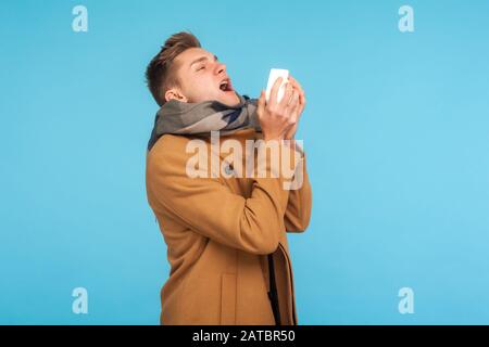 Saison grippale. Homme malade malsain de la grippe en automne manteau et écharpe éternuer fortement dans les tissus, se sentir mal avec le nez liquide, a attrapé froid ou allergie Banque D'Images