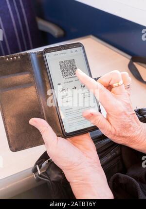 Les mains d'une femme tenant un smartphone affichant un billet de train électronique code QR à bord d'un train, Angleterre, Royaume-Uni Banque D'Images