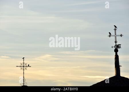 silhouette de deux croix de métal différentes avec des oiseaux perchés sur eux au coucher du soleil et une girouette de temps pointant vers le plus éloigné Banque D'Images