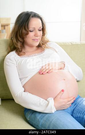 Bonne femme enceinte assise sur le canapé à la maison. Le neuvième mois de grossesse. Banque D'Images