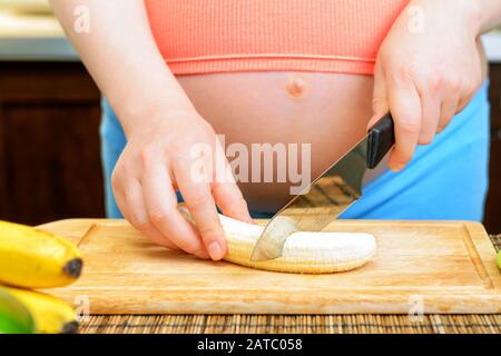 La femme enceinte prépare une banane dans la cuisine Banque D'Images