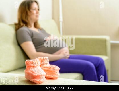 Des chaussons en laine sur le canapé à côté d'une femme enceinte Banque D'Images