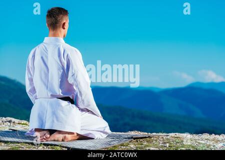 Maître de karaté de méditer au sommet d'une montagne portant des kimono tout en regardant le lac de montagne. Banque D'Images