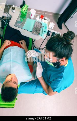 Un jeune garçon de patient est assis dans une chaise de dentiste et un dentiste de sexe masculin examine ses dents Banque D'Images