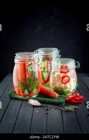 Trois pots de verre de choux-fleurs, concombres fermentés, les carottes, le piment, les épices, le sel. des légumes sur un fond sombre. à l'aide de vert textile ferme. Banque D'Images