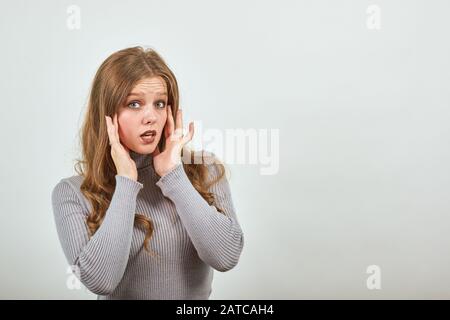 Une jeune fille belle avec des cheveux rouges dans le chandail gris mettre les mains sur ses oreilles Banque D'Images