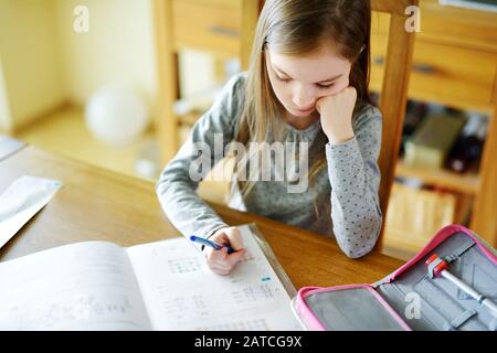 Une petite écolière intelligente qui fait ses devoirs à sa table à la maison. Apprentissage de l'enfant à écrire et à lire. Éducation et apprentissage pour les enfants. Banque D'Images