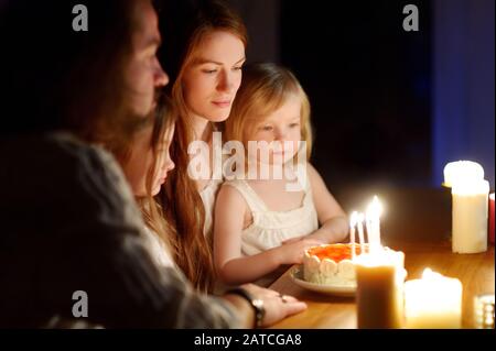 Jeune femme qui fait un souhait avant de souffler des bougies sur son gâteau d'anniversaire. Famille célébrant la fête des oiseaux. Traditions d'anniversaire. Banque D'Images