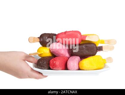 Une main de femme caucasienne tenant une plaque de bonbons colorés couverts de pakes popsicles sur une plaque blanche alternant les saveurs et la direction des cake pop, isolé Banque D'Images