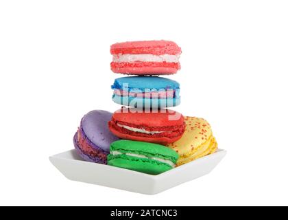 Gros plan sur les cookies Macaron dans différentes couleurs de printemps empilés sur une petite plaque blanche carrée isolée sur fond blanc. Un vrai plaisir français. Banque D'Images