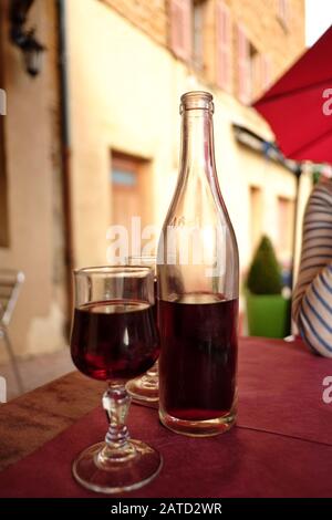 Une bouteille claire et non étiquetée de Beaujolais rouge produit localement sur une table de bistro en plein air avec deux verres de vin un jour d'été à Bagnols France Banque D'Images