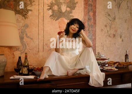 Une belle femme chinoise en coton blanc avec une pâte à noeud à la main, une ambiance festive assise sur une longue table ancienne bénéficie des belles choses dans la vie Banque D'Images