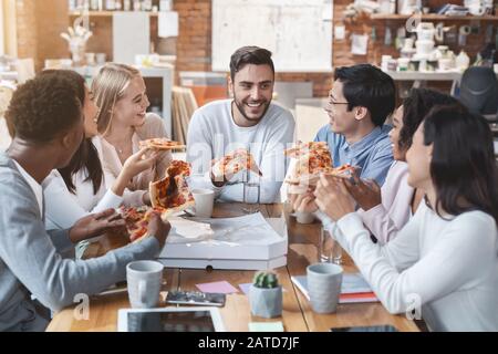 Jeunes collègues déjeuner au bureau, manger de la pizza Banque D'Images