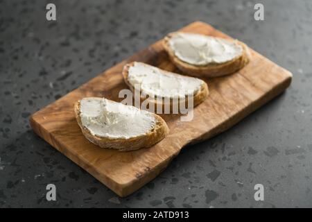Trois tranches de pain ciabatta avec fromage à la crème sur le bois d'olive sur la surface du sol en terrazzo, accent peu profondes Banque D'Images