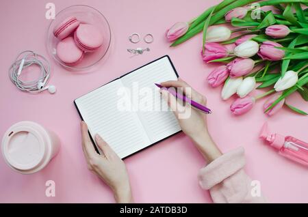Fille écrivant la liste de souhaits pour les plans futurs. Composition plat de laïcs avec des fleurs, bloc-notes, une tasse de café et des bonbons Banque D'Images