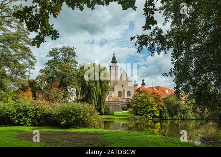 Telc / République tchèque - 27 septembre 2019: Vue sur une église de James le Grand depuis un jardin de château au-dessus d'un lac avec des canards encadrés d'arbres verts. Banque D'Images