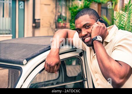 Jeune afro américain gars parlant au téléphone portable suivant ancienne voiture rétro - Noir homme souriant pendant la conversation téléphonique - mode avec de nouvelles tendances concept - Banque D'Images