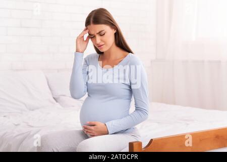 Femme Enceinte Mal Assise Sur Lit Intérieur Banque D'Images