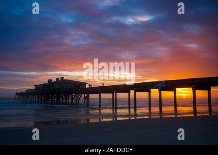 Daytona Beach, FL/USA-Dec 29, 2019: Un restaurant situé sur une jetée de pêche est silhouetté contre la lueur d'un lever de soleil sur l'horizon de l'Atlant Banque D'Images