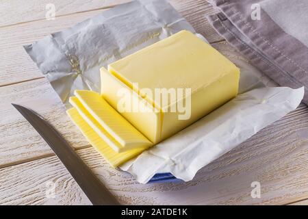 Tranches de beurre jaune frais coupées à partir d'un paquet ouvert et couteau sur une table en bois blanc. Produits Laitiers. Beurre sandwich. Éléments nutritifs naturels de la graisse. Banque D'Images