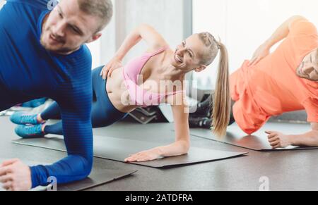 Une femme et des hommes de forme physique dans le club de santé faisant une planche latérale Banque D'Images