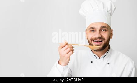 Le Chef Guy Tasting Dish Holding Spoon Pose Sur Fond Gris Banque D'Images