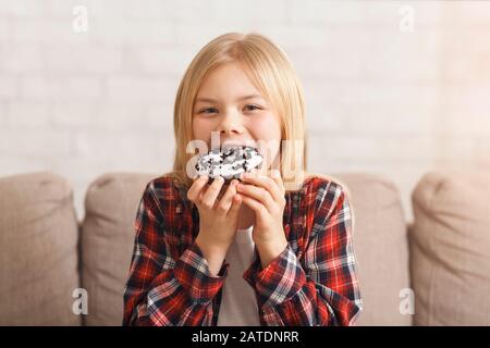 Une Fille Qui Aime Manger Un Donut Malsain Assis Sur Un Canapé À La Maison Banque D'Images