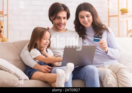 Famille Caucasienne Et Gaie Assise Sur Un Canapé Avec Ordinateur Portable Et Carte De Crédit Banque D'Images
