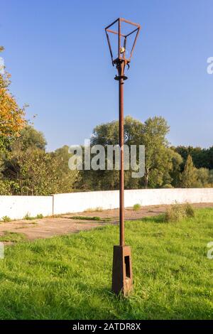 Ancienne lampe de rue avec ampoule cassée et fils électriques déchirés sur poteau en métal rouillé dans la zone de parc abandonné contre fond de ciel bleu brillant, gr Banque D'Images