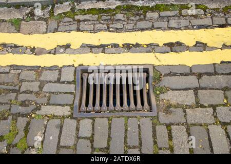 Gros plan sur les drains métalliques et les doubles lignes jaunes sur le côté de la route pavée, Edimbourg, Ecosse, Royaume-Uni Banque D'Images