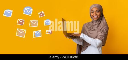 Happy Black Muslim Woman Avec Ordinateur Portable Et Enveloppes Volantes Sur Fond Banque D'Images