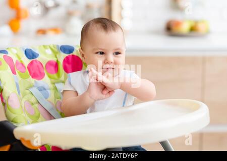 Joyeux bébé qui claque les mains, assis dans la chaise haute dans la cuisine Banque D'Images