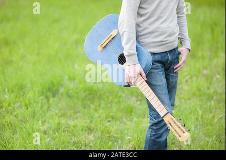 homme en sweat-shirt et jeans tenant la guitare personnalisée vintage debout sur l'herbe verte avec copyspace Banque D'Images